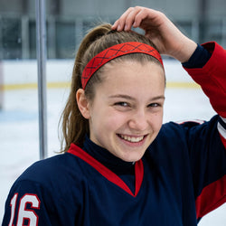 Woman wearing a red headband with a hockey pattern, looking off to the side.