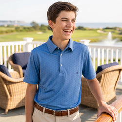 Young man wearing a blue polo shirt standing outdoors with a scenic background