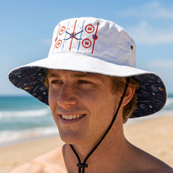 Man wearing a white bucket hat with red and blue hockey design on a beach.