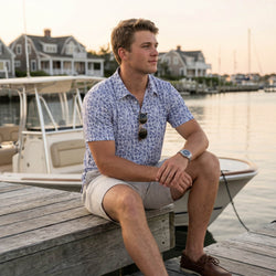 Teen wearing a hockey patterned polo shirt outdoors by a dock.