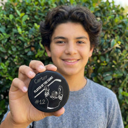 Person holding a 'Player of the Game' puck with text and graphics, outdoors.