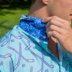 Close-up of a man wearing a light blue short-sleeve button-up shirt with a red and blue hockey stick pattern, adjusting the collar which features a blue pattern of white and pink hockey sticks.