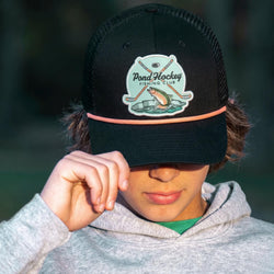Person wearing a black cap with a 'Pond Hockey Fishing Club' logo, blurred background