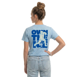Person wearing a light blue t-shirt with a hockey graphic and text on the back, standing against a white background.