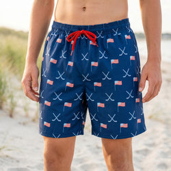 Person wearing blue swim shorts with hockey and American flag pattern on a beach.
