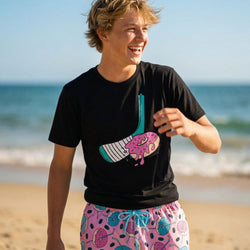 Teenage boy wearing a black t-shirt with a colorful hockey donut graphic on a beach