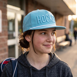Person wearing a light blue 'Hockey' cap outdoors