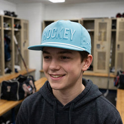 Person wearing a blue 'HOCKEY' cap in a locker room setting