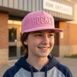 Person wearing a pink 'HOCKEY' cap in front of a building