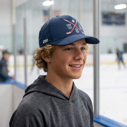 Person wearing a blue cap with a hockey logo on an ice rink