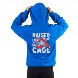 Royal blue hoodie with 'Raised in Cage' graphic on the back, worn by a person.