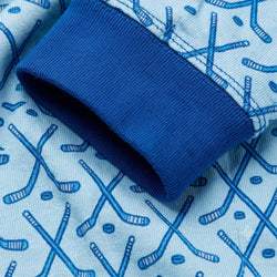 Close-up of a light blue fabric cuff with a dark blue ribbed knit edge, featuring a repeating pattern of crossed hockey sticks and hockey pucks.