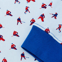 A close-up of a lighblue fabric garment featuring a repeating pattern of red and navy hockey players, with a folded cuff showing a solid royal blue ribbed edge.