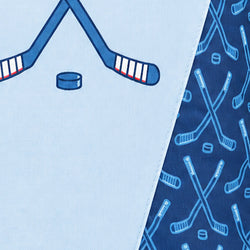 Close-up of a light blue fabric product with a hockey theme, showing crossed hockey sticks, a hockey puck, and a darker blue patterned section with repeated hockey stick and puck motifs.
