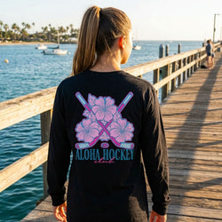 Person wearing a black long-sleeve shirt with 'Aloha Hockey Club' design by the water.