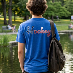Person wearing a blue 'Hockey' t-shirt in a park setting with a pond and trees.
