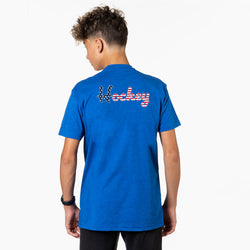 Person wearing a blue t-shirt with a patriotic hockey script text on the back, standing against a white background