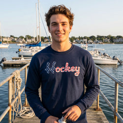 Person wearing a navy blue sweatshirt with 'Hockey' printed on it, standing on a dock with boats in the background.