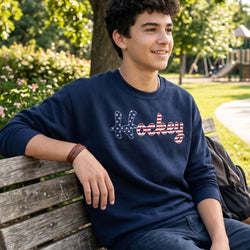 Person wearing a navy blue sweatshirt with 'Hockey' printed on it, sitting on a wooden bench in a park.