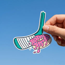 Hand holding a colorful hockey stick with donut sticker against a blue background