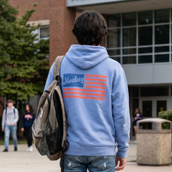 Person wearing a blue hoodie with an American flag design, standing outside a building.