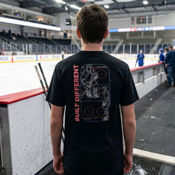 Person wearing a black t-shirt with a hockey design and text at an indoor hockey facility.