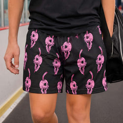 A person wearing black athletic shorts with a repeating pink skull-and-hockey pattern, paired with a black top and carrying a black bag, photographed indoors on a paved surface.