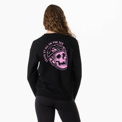 A woman shown from the back wearing a black sweatshirt with a large pink graphic of a skull in a hockey helmet and the text 'LEAVE IT ALL ON THE ICE' printed on the back, paired with black leggings against a plain white background.