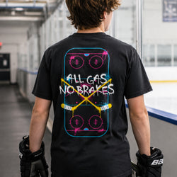 A person viewed from behind wearing a black graphic T-shirt with a hockey-themed back print reading 'ALL GAS NO BRAKES' over a stylized rink graphic. The person is standing in an indoor rink or sports facility with ice visible in the background.