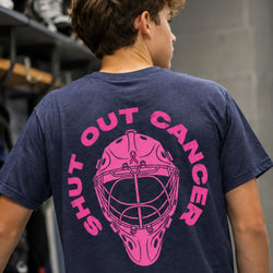 A person shown from behind wearing a navy blue t-shirt with a bright pink graphic of a hockey goalie mask and the words 'SHUT OUT CANCER' printed on the back.
