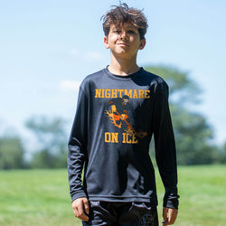 A young boy wearing a black long-sleeve graphic shirt with 'NIGHTMARE ON ICE' and a hockey player illustration in yellow and orange, standing outdoors in a grassy field under a blue sky.