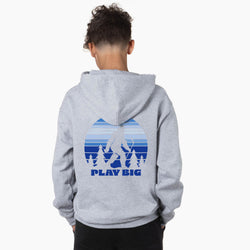 A child viewed from behind wearing a heather gray hoodie with a blue graphic of a Bigfoot silhouette against a striped sunset and the text 'PLAY BIG' on the back.