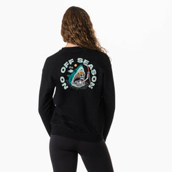 A woman viewed from the back wearing a black crewneck sweatshirt with a large graphic on the back. The graphic features the text 'NO OFF SEASON' in white around a cartoon shark with a skeleton holding a hockey stick coming out of its mouth.