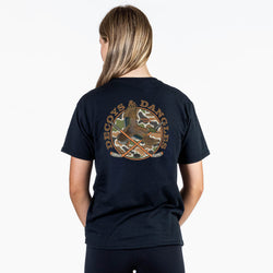 A girl viewed from behind wearing a black tee with a large graphic on the back. The graphic features the words 'DECOYS & DANGLES' in a tan font surrounding a camouflage-patterned circle with a duck and crossed hockey sticks
