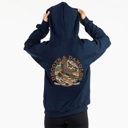 A girl viewed from behind wearing a navy sweatshirt with a large graphic on the back. The graphic features the words 'DECOYS & DANGLES' in a tan font surrounding a camouflage-patterned circle with a duck and crossed hockey sticks