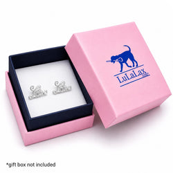 A pair of silver script stud earrings spelling out 'Lax' in cursive, presented in an open pink gift box with a navy blue interior. The lid of the box is propped up, showing the blue printed brand logo 'LulaLax'.