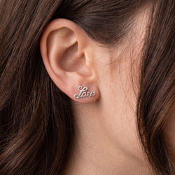 A close up of a girl wearing silver earrings with the word 'Lax' in a script style.
