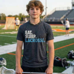 Boy wearing a 'Eat. Sleep. Lacrosse.' shirt on a lacrosse field