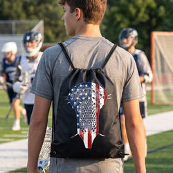 Person wearing a black patriotic lacrosse themed drawstring backpack on a lacrosse field.