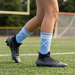 Person wearing blue socks with white lacrosse designs on a grassy field
