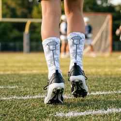 Person wearing white camo socks with black patterns and black cleats on a grassy field.