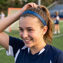 Woman adjusting her blue lacrosse headband on a sports field