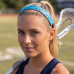 Woman wearing a blue headband with a lacrosse stick in the background