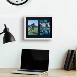 Dear Dad Girls Lacrosse wooden frame featuring a picture of a girl playing lacrosse hanging on a wall above a computer
