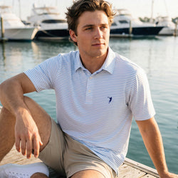 Teen wearing a lacrosse polo shirt out doors by a pier.