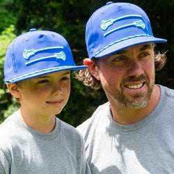 Father and son wearing matching blue lacrosse rope hats featuring embroidered crossed sticks.