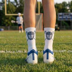 Person wearing white socks with lacrosse helmet designs on a grassy field.