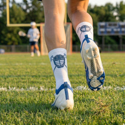 Person wearing white socks with lacrosse helmet on a grassy field.