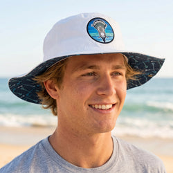 Man wearing a white bucket hat with a lacrosse logo on a beach