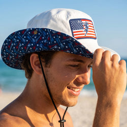 Man wearing a white bucket hat with American flag design on a beach